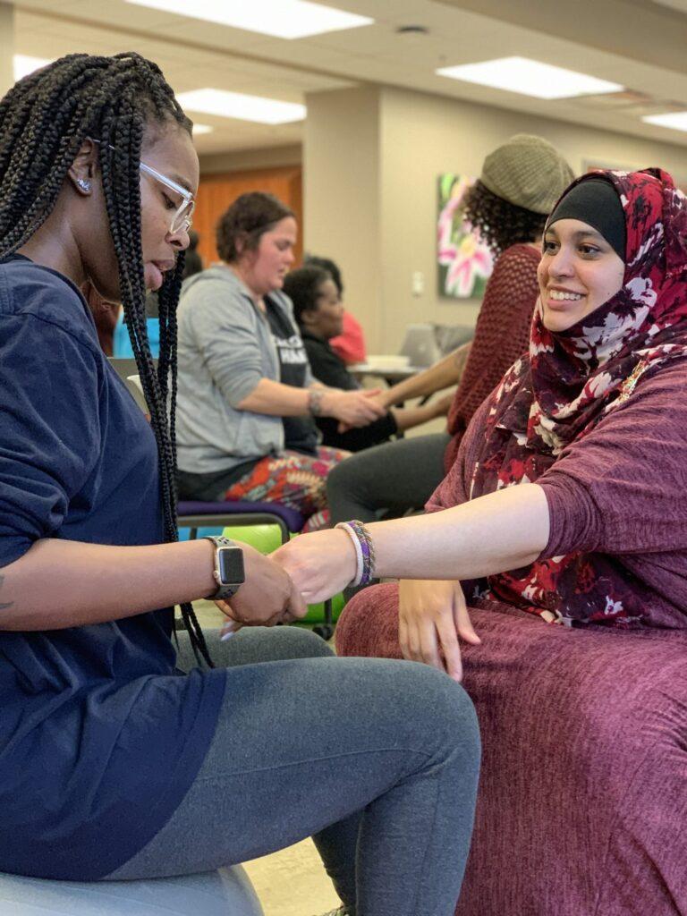 A woman in a hijab shakes hands with another woman in a classroom.