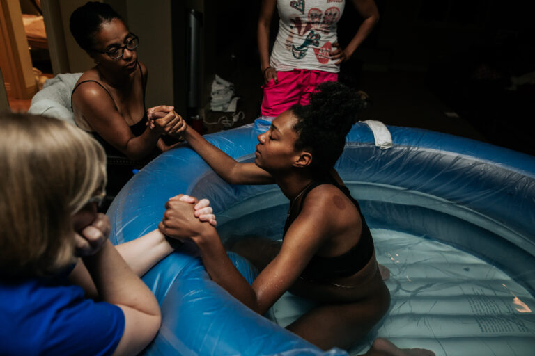 Two women holding the hands of a laboring person in the blue birth pool
