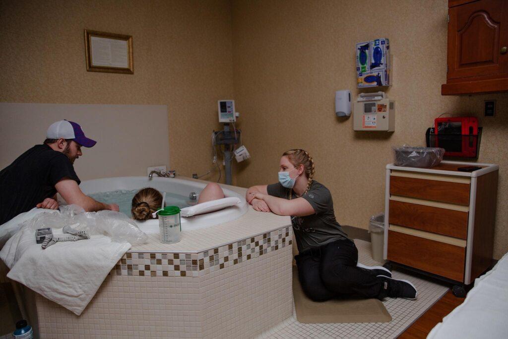 A doula sits next to a tub while a person is in labor.