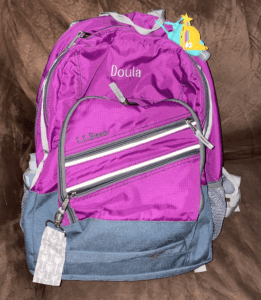 A magenta back pack with the word DOULA embroidered on it.