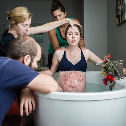 Pregnant woman in a tub of water, surrounded by her doula and partner