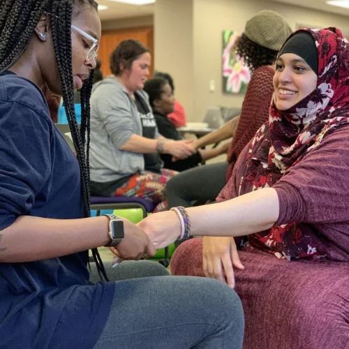 A woman in a hijab shakes hands with another woman in a classroom.