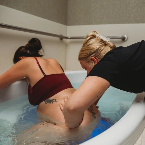 A doula gives double hip squeezes in the water birth tub